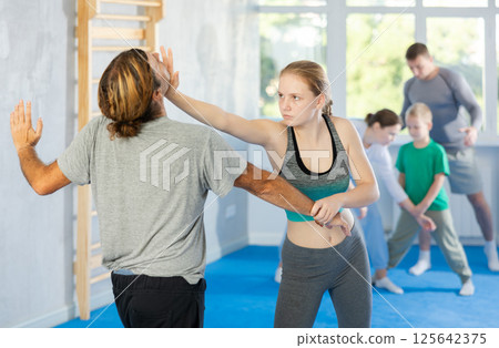 Girl and man in group self-defense classes practicing sparring technique of blowing to chin in gym 125642375