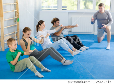 Group of people performing combat strikes sitting during group training Group of people performing combat strikes sitting during group training 125642416