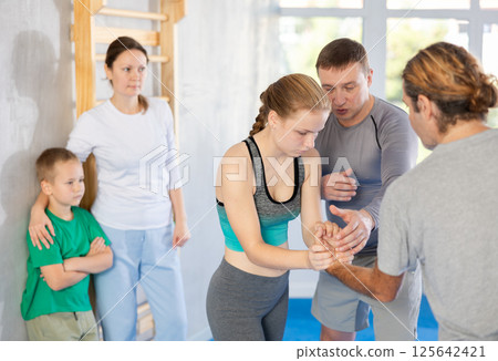 Trainer on man explains palm grab technique, boy, girl and woman watch and learn Trainer on man explains palm grab technique, boy, girl and woman watch and learn 125642421