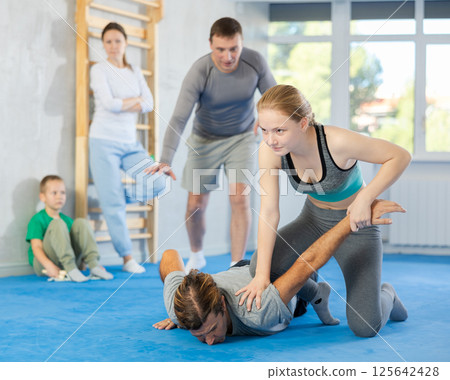 At self-defense training, trainer teaches teenage girl technique of grabbing arm and lowering opponent to floor 125642428
