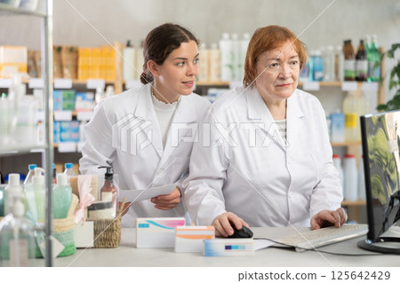 Two pharmacists working at a computer in a pharmacy 125642429