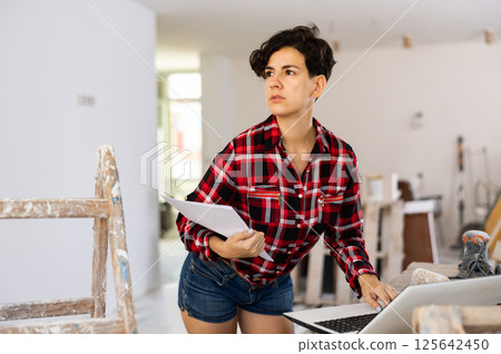 Woman builder checking project documentation and using laptop while working Woman builder checking project documentation and using laptop while working 125642450