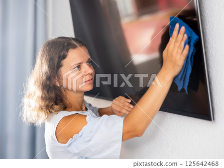 Young woman cleaning TV screen at home Young woman cleaning TV screen at home 125642468