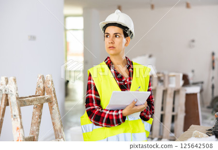 Focused young female civil engineer making notes at construction site indoors Focused young female civil engineer making notes at construction site indoors 125642508