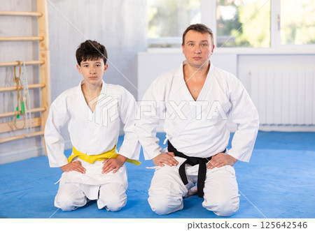 Teenage boy and middle-aged man wearing kimono sitting in seiza position in sports hall Teenage boy and middle-aged man wearing kimono sitting in seiza position in sports hall 125642546