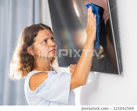 Housewife wipes dust from the TV at home with rag Housewife wipes dust from the TV at home with rag 125642569