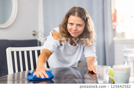 Positive brunette woman cleaning table at home Positive brunette woman cleaning table at home 125642582