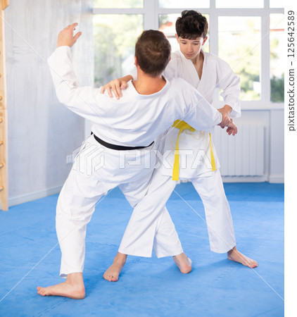 Teenage boy applying judo techniques on middle-aged trainer during sports classes 125642589