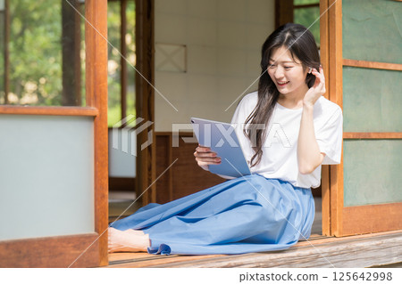 年輕女子一邊笑著一邊看著平板電腦，一邊把頭髮往後梳 125642998