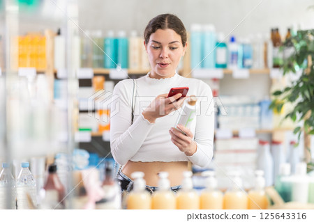 Girl in summer clothes scans code on medicinal shampoo to check expiration date 125643316