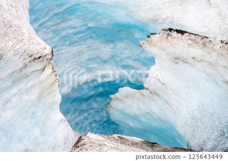 Crevasse in the ice from melting at Athabasca Glacier in Jasper National Park with cloudy sky 125643449