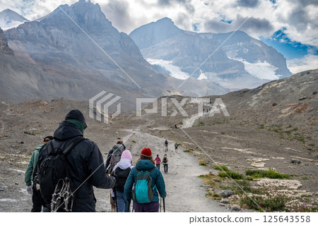 Line of tourist hikers heading up to the Athabasca Glacier in Jasper National Park with cloudy sky 125643558