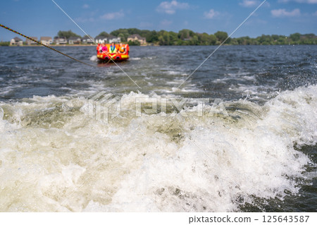 Inflatable raft being pulled at a high speed by a boat in a recreational activity called tubing Inflatable raft being pulled at a high speed by a boat in a recreational activity called tubing 125643587