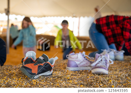 Selective focus on shoes on a straw bale with a corn and children in the background. Selective focus on shoes on a straw bale with a corn and children in the background. 125643595