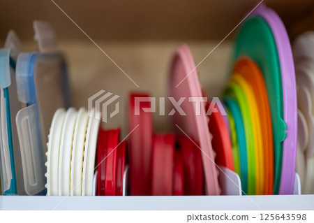 Narrow depth of field picture of an open kitchen cabinet with rows of organized storage of plastic lids. 125643598