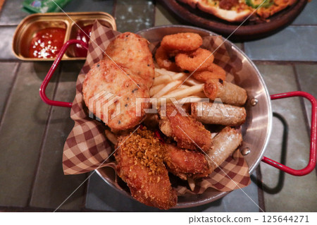 close up of assorted Thai appetiser including stir fried fishcake, round patties, french fries, onion rings, spring rolls, and chicken wings in a metal basket with sweet and sour sauce  125644271