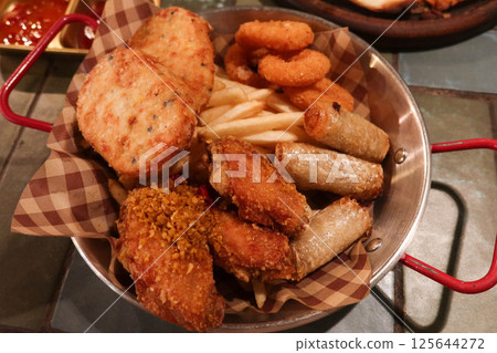 close up of assorted Thai appetiser including stir fried fishcake, round patties, french fries, onion rings, spring rolls, and chicken wings in a metal basket with sweet and sour sauce close up of assorted Thai appetiser including stir fried fishcake, round patties, french fries, onion rings, spring rolls, and chicken wings in a metal basket with sweet and sour sauce 125644272