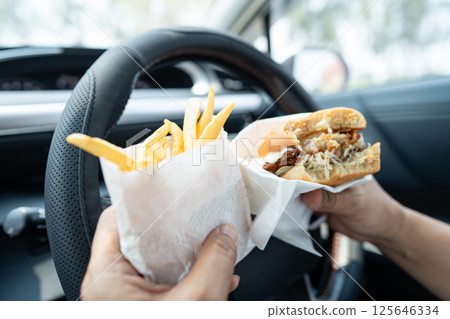 Asian lady holding hamburger to eat in car, dangerous and risk an accident. 125646334