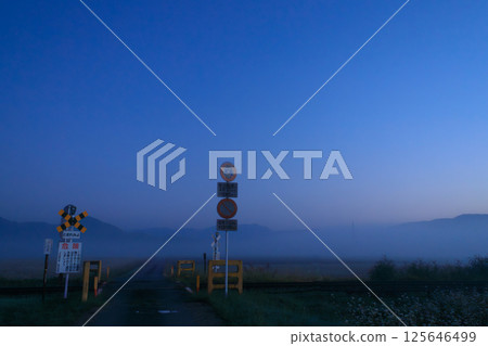 A railroad crossing shrouded in morning mist awaits the first train on the Echigo-Mie Line. 125646499