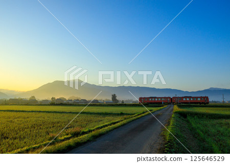 The orange diesel train of the Etsumi-Hoku Line runs through the railroad crossing with the watchful eye of Mount Arashiyama. The orange diesel train of the Etsumi-Hoku Line runs through the railroad crossing with the watchful eye of Mount Arashiyama. 125646529