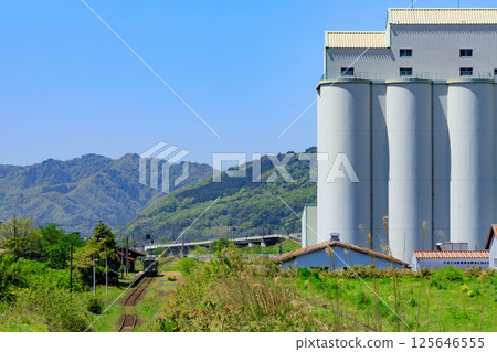 A Wakasa Railway diesel train parked at an unmanned station next to a huge grain warehouse 125646555