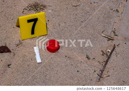 One yellow crime scene marker on the paving slab near a bottle cap and a cigarette butt One yellow crime scene marker on the paving slab near a bottle cap and a cigarette butt 125648617