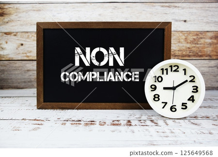 Non Compliance text message and alarm clock on wooden background 125649568