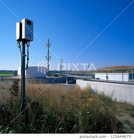 Modern Wastewater Treatment Plant Facility under a Clear Blue Sky pipes metal grass weeds sunny 125649679