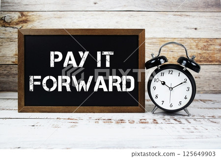 Pay It Forward text message and alarm clock on wooden background 125649903