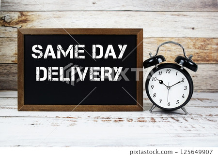 Same Day Delivery text message and alarm clock on wooden background 125649907