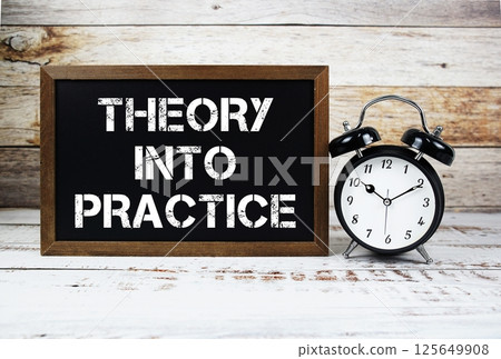 Theory Into Practice text message and alarm clock on wooden background Theory Into Practice text message and alarm clock on wooden background 125649908