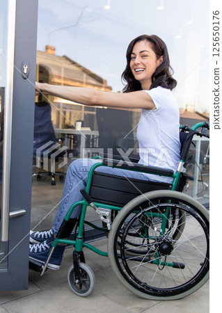 Dark-haired woman on a wheelchair at the office entrance 125650176