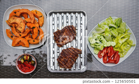 Grilled butternut squash and pork cuts, some fresh vegetable next to it, on glass garden table, view from above 125650501