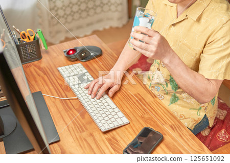 A man holding a glass cup while typing on a keyboard 125651092