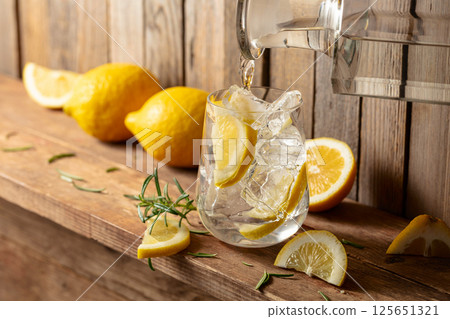 Summer refreshing drink with ice, rosemary and lemon slices on a old wooden table. Summer refreshing drink with ice, rosemary and lemon slices on a old wooden table. 125651321