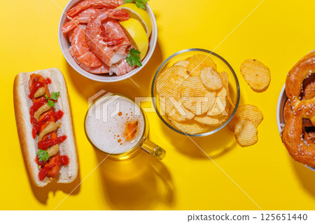 A vibrant photo showcasing a glass of beer surrounded by various snacks and fast food 125651440