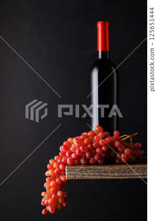 A bottle of wine paired with grapes, set against a dark background A bottle of wine paired with grapes, set against a dark background 125651444