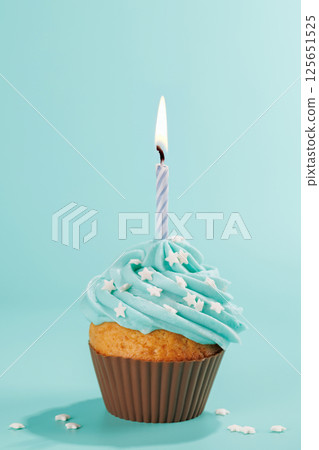 Festive cupcake topped with swirled frosting and a lit candle Festive cupcake topped with swirled frosting and a lit candle 125651525