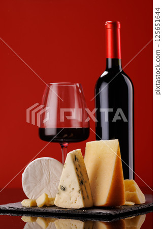 A refined selection of aged cheeses presented on a board, accompanied by a glass of wine 125651644