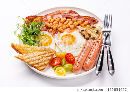 A classic breakfast plate featuring sunny-side-up eggs, crispy bacon, sausages, and fresh tomatoes 125651652
