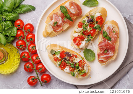 Tasty antipasto toasts featuring classic caprese with mozzarella and tomatoes, and savory prosciutto with herbs Tasty antipasto toasts featuring classic caprese with mozzarella and tomatoes, and savory prosciutto with herbs 125651676