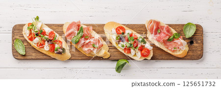 Tasty antipasto toasts featuring classic caprese with mozzarella and tomatoes, and savory prosciutto with herbs 125651732