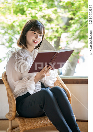 A young woman reading a book in a room with a view of fresh greenery A young woman reading a book in a room with a view of fresh greenery 125651985