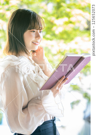 A young woman reading a book among the fresh greenery A young woman reading a book among the fresh greenery 125652073