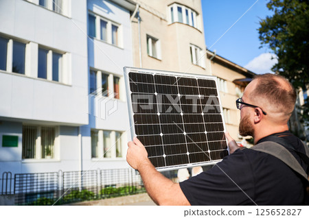 Man holding photovoltaic solar panel in front of historical building. Concept of integration of sustainable renewable energy sources into architecture. 125652827