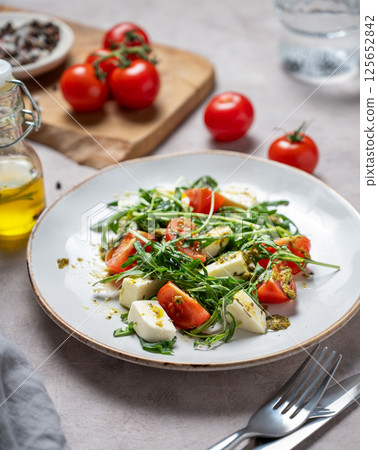 Healthy arugula salad with cherry tomatoes, mozzarella and pesto sauce on a light background 125652842