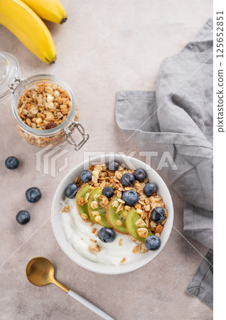 Natural greek yogurt with granola, kiwi and blueberries in a bowl on a light background Natural greek yogurt with granola, kiwi and blueberries in a bowl on a light background 125652851