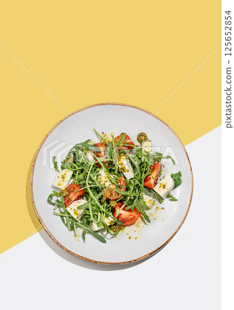 Fresh arugula salad with cherry tomatoes, mozzarella, pesto sauce on white yellow background. Fresh arugula salad with cherry tomatoes, mozzarella, pesto sauce on white yellow background. 125652854