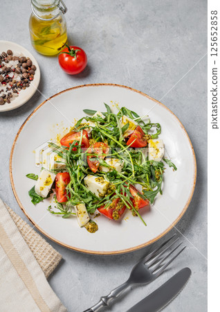 Arugula salad with cherry tomatoes, mozzarella and pesto sauce on a light background Arugula salad with cherry tomatoes, mozzarella and pesto sauce on a light background 125652858