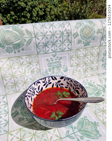 Delicious borscht served in a decorative bowl, showcasing Ukrainian beetroot soup with fresh herbs garnish against a patterned tablecloth 125653034